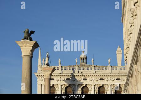 Guardando le colonne, il Leone di San Marco e San Teodoro e le statue sulla balaustra, la Biblioteca Nazionale Marciana contro un cielo blu Foto Stock