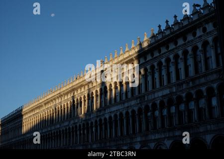 La lunga facciata delle Procuratie vecchie, lato nord della piazza, architettura rinascimentale italiana del XVI secolo con luce mattutina, luna e cielo blu Foto Stock