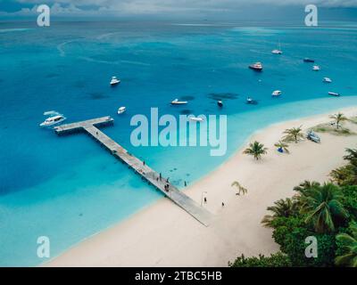 Vista aerea della paradisiaca spiaggia tropicale delle Maldive con molo e motoscafi sull'isola. Concetto di vacanza estiva e di viaggio. Foto Stock