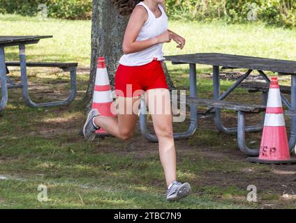 Una donna con pantaloncini rossi e canotta bianca che corre una gara di 5K in un parco. Foto Stock