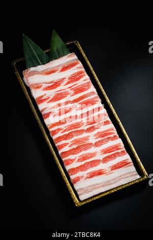 Affettato di maiale crudo e striato in un piatto bianco per lo Yakiniku, il Sukiyaki, il barbecue e lo Shabu. Foto Stock