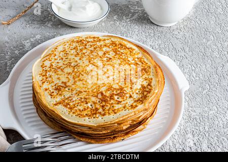 Pila di pancake appena fatti su un piatto bianco di ceramica su sfondo grigio cemento. Una delizia tradizionale per il Festival di Primavera in Russia Foto Stock