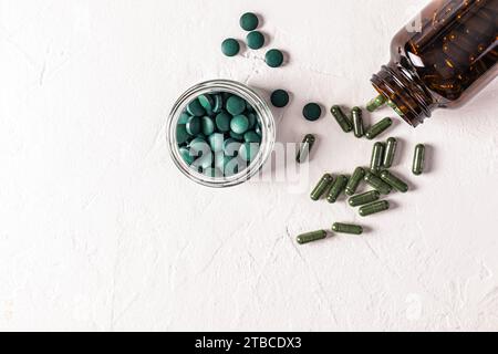 Compresse di alghe spirulina naturali rotonde, blu-verdi, in recipiente su sfondo bianco. vaso medico con capsule di alghe. Integratori alimentari naturali. Foto Stock