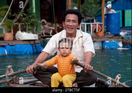 Fisherman e suo figlio si avvicinarono al canottaggio ormeggiato fuori dalla loro casa galleggiante nella baia di ha Long Foto Stock