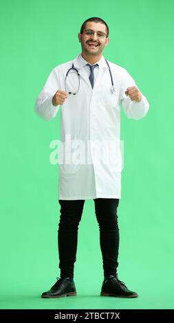 un medico maschio con un cappotto bianco su sfondo verde si rallegra. alzò le mani Foto Stock