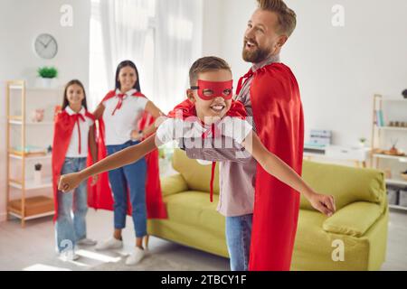 Sorridente famiglia di quattro persone con costumi da supereroe rossi che giocano a giocare immagina di volare a casa. Foto Stock