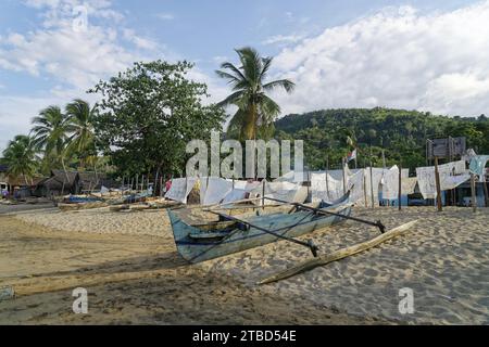 Barca da pesca sulla spiaggia, coperte decorative ricamate, palme, Ampangorinana, Nosy Komba, Madagascar Foto Stock