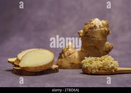 Tritare lo zenzero in un cucchiaio di legno con radice di zenzero fresca tagliata a fette Foto Stock