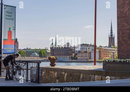 Pittoresca vista degli edifici storici nel centro di Stoccolma dalla riva opposta. Il ciclista sta parcheggiando la sua bicicletta sul ponte, aggiungendo un tocco di fascino urbano Foto Stock