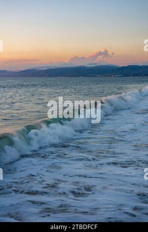 Le onde si infrangono al tramonto con le montagne di Santa Monica e Malibu sullo sfondo Foto Stock