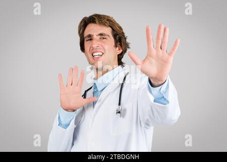 Medico maschile che mostra il gesto di stop con entrambe le mani, guardando stressato Foto Stock