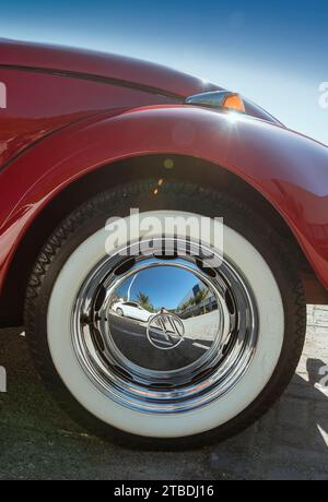 Ruota di una Volkswagen Beetle rossa. Pneumatico con striscia bianca e coprimozzo cromato che si illumina nelle giornate di sole con il cielo blu. Foto Stock