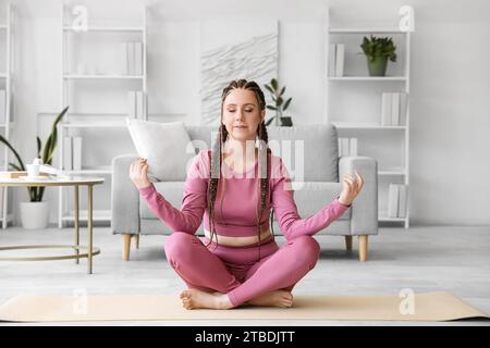 Giovane donna con dreadlock che meditava a casa Foto Stock