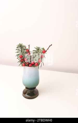 Bouquet di nobilis abete e rami di winterberry in un vaso d'epoca di fronte a sfondo beige. Concetto natalizio con spazio per la copia. Foto Stock