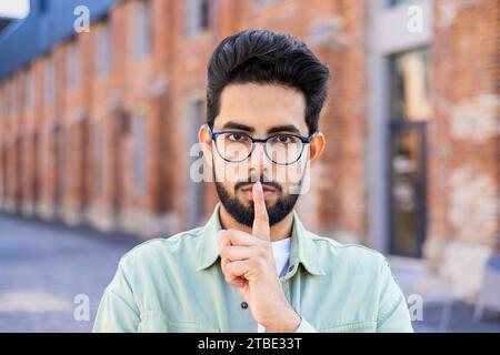 Un giovane indiano sta per strada, mette il dito indice sulle labbra, guarda la telecamera. Foto Stock
