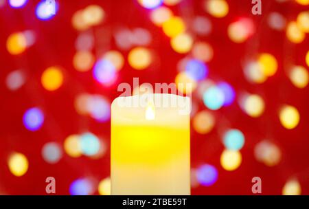 Candela accesa su uno sfondo non a fuoco con luci su sfondo rosso Foto Stock