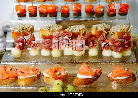 Un delizioso assortimento di tartine, tra cui salmone affumicato, prosciutto con melone e vari condimenti su un vassoio da portata in vetro Foto Stock