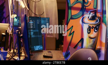 Graffiti ha dipinto una base nascosta vuota con righe di codice in esecuzione sullo schermo del computer con malware che superano i sistemi di sicurezza. PC in bunker deserto che mostrano script in grado di hackerare i dispositivi Foto Stock