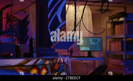 Ingrandire i computer con tecnologia avanzata lasciando aperto il codice in esecuzione in un seminterrato vuoto illuminato al neon con disegni di graffiti dipinti sulle pareti. Apparecchiature high-tech utilizzate dagli hacker nei magazzini sotterranei Foto Stock