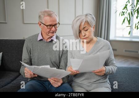 Triste stanco, deluso, coppia di anziani di mezza età siedono con un documento cartaceo. Infelice anziano maturo donna che legge banconote che gestiscono le finanze bancarie calcolano le tasse pianificazione prestito pagamento pensione Foto Stock