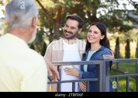 Rapporto amichevole con i vicini. Coppia felice e uomo anziano vicino alla recinzione all'aperto Foto Stock