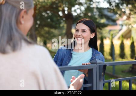 Rapporto amichevole con i vicini. Donne felici vicino alla recinzione all'aperto Foto Stock