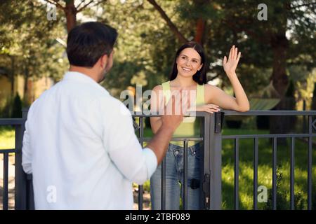 Rapporto amichevole con i vicini. Donna felice che saluta l'uomo vicino alla recinzione all'aperto Foto Stock