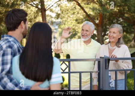 Rapporto amichevole con i vicini. Coppie anziane salutano giovani famiglie vicino a recinzioni all'aperto Foto Stock