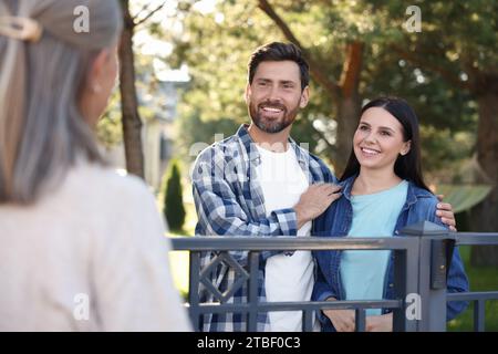 Rapporto amichevole con i vicini. Felice giovane coppia e donna anziana vicino a recinzione all'aperto Foto Stock