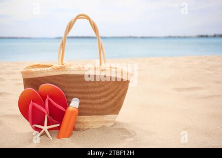 Borsa di paglia, infradito, stelle marine e crema solare sulla spiaggia, spazio per il testo Foto Stock