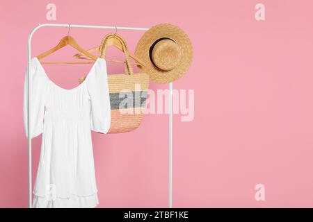 Rack con accessori ed elegante abito bianco su appendiabiti in legno su sfondo rosa, spazio per il testo Foto Stock