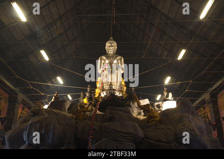 Una grande statua di Buddha seduto in argento nella posa Pa Lelai. All'interno della sala dei sermoni in fondo, i devoti possono passarci sotto. Al tempio di Wat Tha mai. Foto Stock