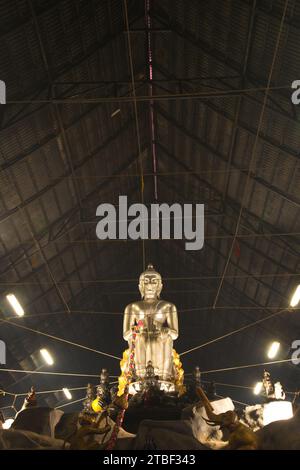 Una grande statua di Buddha seduto in argento nella posa Pa Lelai. All'interno della sala dei sermoni in fondo, i devoti possono passarci sotto. Al tempio di Wat Tha mai. Foto Stock