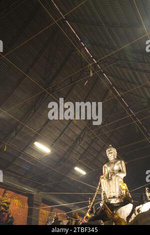 Una grande statua di Buddha seduto in argento nella posa Pa Lelai. All'interno della sala dei sermoni in fondo, i devoti possono passarci sotto. Al tempio di Wat Tha mai. Foto Stock