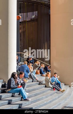 Giovani felici seduti (lavoratori d'ufficio) al sole di mezzogiorno d'inverno sui gradini dell'8 Chifley Square, grattacielo di Sydney in Australia Foto Stock