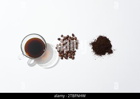 Una tazza di caffè nero, chicchi di caffè e polvere di caffè disposti in modo ordinato su uno sfondo bianco. Bere il caffè è efficace nel prevenire e ridurre il t Foto Stock