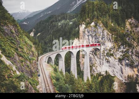 Treno rosso svizzero sul viadotto in montagna, giro panoramico Foto Stock