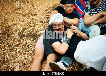 Festival di musica, amici in costume ed evento con un gruppo di giovani al piano terra all'aperto dall'alto. Festa, estate e uomini sdraiati per terra Foto Stock
