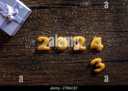 2024, l'anno 2024 scritto in lettere di pane su uno sfondo di motivi di legno. Foto Stock