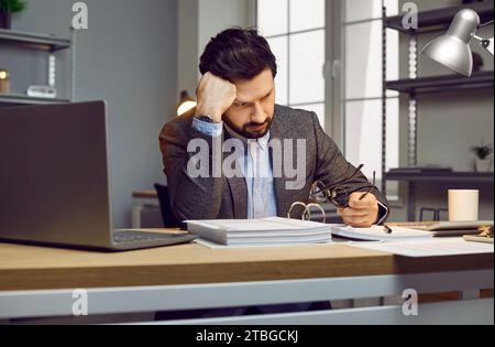 Il revisore o contabile maschio si stanca mentre lavora con i documenti in ufficio Foto Stock