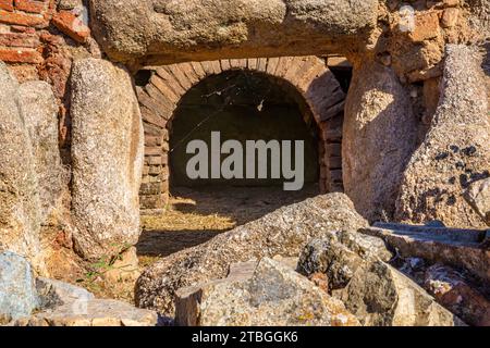 Rovine di una porta esterna ad arco in mattoni di una sala di gladiatori o gabbie di bestie nell'anfiteatro Merida, fatta di blocchi di roccia e mattoni con una sabbia e. Foto Stock