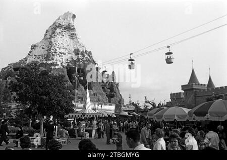 Zahlreiche Besucher erfreuen sich an Disneyland, rechts das Matterhorn in der Version von 1959-1978 sowie zwei Gondeln des Skyway, mittig im Hintergrund der Eingang zum Bereich Alice im Wunderland, dessen Mauern und Spitzdächer rechts sichtbar sind, Anaheim 1962. Numerosi visitatori apprezzano Disneyland, sulla destra il Cervino nella versione 1959-1978 e due gondole della Skyway, sullo sfondo centrale l'ingresso all'area di Alice nel Paese delle meraviglie, le cui pareti e tetti a punta sono visibili sulla destra, Anaheim 1962. Foto Stock