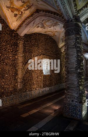 Colonna coperta e decorata con ossa umane e teschi e soffitto a volta con dipinti allegorici religiosi della Cappella delle ossa illuminata Foto Stock