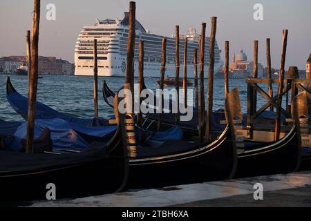 Una gigantesca nave da crociera entra nel canale di Guidecca che domina Redentore e le gondole sulle acque blu al Molo di Riva degli Schiavoni, il turismo di massa a Venezia Foto Stock