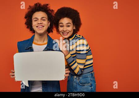 fratello e sorella afro-americani affezionati in posa con bolla di discorso sullo sfondo arancione Foto Stock