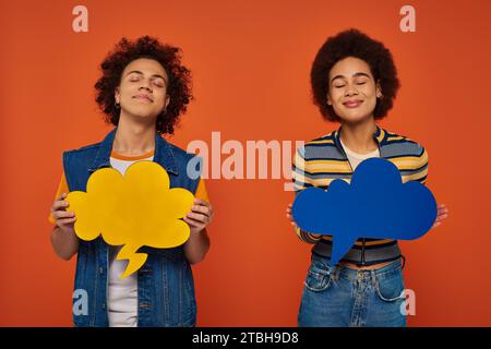 fratello e sorella afro-americani dall'aspetto gradevole che si mettono in posa con bolle di pensiero sullo sfondo arancione Foto Stock