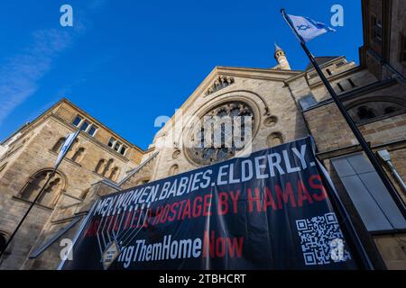 Colonia, Germania. 7 dicembre 2023. Uno striscione con la scritta 'uomini. Donne. Bambini. Anziani. Sono ancora tenuti in ostaggio dagli stand di Hamas davanti a un candelabro Hanukkah di fronte alla sinagoga. Hanukkah, che inizia oggi, è un festival ebraico annuale che dura otto giorni. Crediti: Rolf Vennenbernd/dpa/Alamy Live News Foto Stock