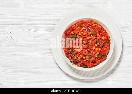 chakalaka tradizionale sudafricano, rinfrescante sapore piccante di fagioli di pomodoro in una ciotola bianca su un tavolo di legno bianco, vista orizzontale dall'alto, piatto, fr Foto Stock