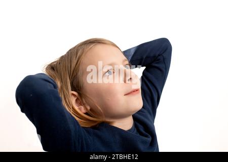 Un ragazzo dai capelli lunghi guarda verso l'alto mentre si stende sulle mani, creando una scena stravagante e contemplativa su uno sfondo bianco pulito. Foto Stock