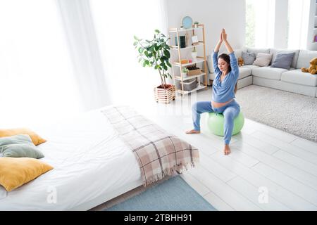 Foto della mamma di una ragazza incinta, tranquilla e sportiva, seduta sul fitball, respirazione profonda e meditazione in camera da letto confortevole e confortevole Foto Stock